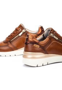 Zapatillas de cuero marrón con un acabado texturizado, que presentan detalles en dorado, cremalleras laterales y una suela de goma blanca.