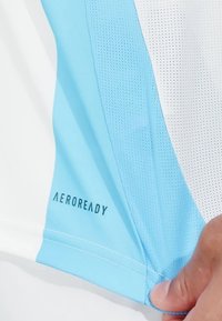 Ljusblå träningströja med vit meshpanel, med "AEROREADY"-logotyp i svart på ärmen. Slät textur, ergonomisk design.