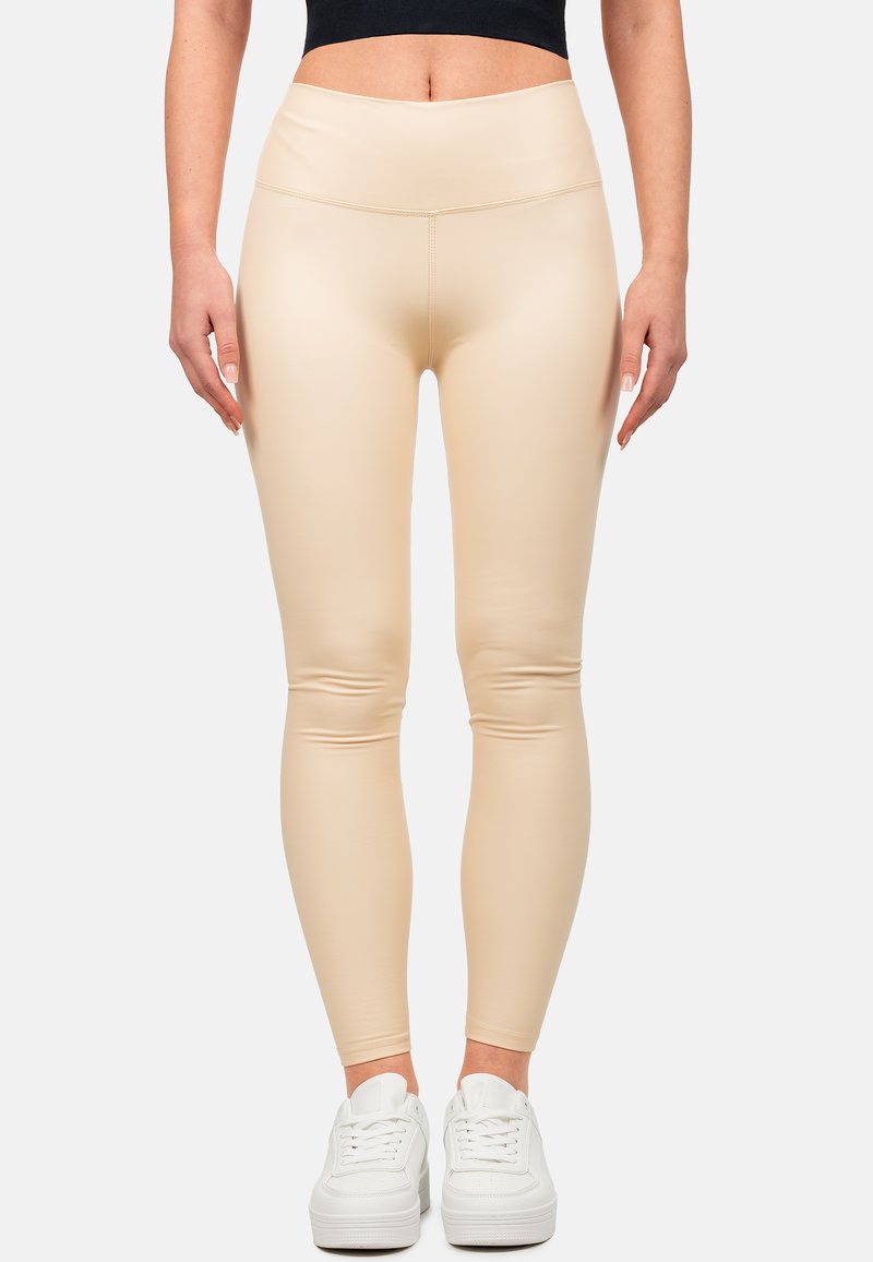 Leggings beige a vita alta realizzati in un materiale morbido ed elastico, con un design aderente. Abbinati a sneakers bianche.