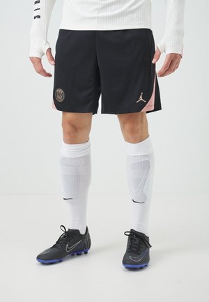 Mand iført sorte Paris Saint-Germain fodboldshorts med hvide sokker og sorte Nike fodboldstøvler på en ensfarvet hvid baggrund.