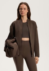 Brun bomberjacka med dragkedja fram, tillsammans med en matchande crop top och högmidjade leggings, alla i ett smidigt, elastiskt tyg.