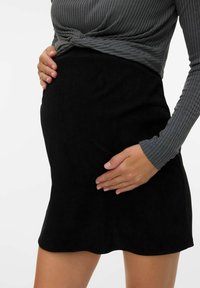 Un haut à manches longues rayé gris, noué à la taille, associé à une jupe en velours côtelé noire. La jupe a une texture lisse et un ourlet en forme de vagues.