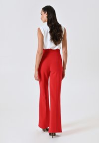 Pantalons rouges évasés à taille haute, fabriqués en tissu lisse. Associés à un haut sans manches blanc. Vue de dos, silhouette épurée, détails minimalistes.