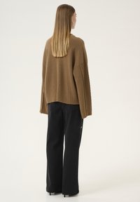 Maglione marrone lavorato a maglia con un design testurizzato, vestibilità ampia e maniche larghe, abbinato a pantaloni neri a gamba larga con tasca laterale.