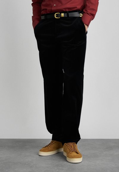 Black velvet pants with a loose fit, featuring side pockets and a black belt with a gold buckle. Paired with tan suede sneakers.