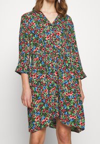 Blommig klänning med svart bakgrund, prydd med röda, blåa och gröna blommor. V-ringad halslinje och trekvartslånga ärmar, med en svängig silhuett.