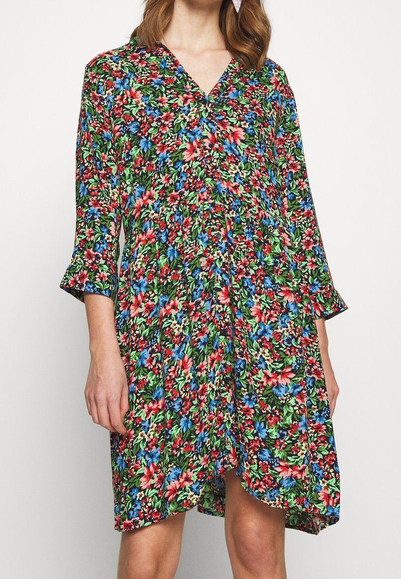 Blommig klänning med svart bakgrund, prydd med röda, blåa och gröna blommor. V-ringad halslinje och trekvartslånga ärmar, med en svängig silhuett.