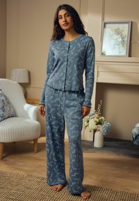 Sinised lillemustriga pyjama pika varrukaga ja elastsete mansettidega, millel on nööpidega eesmine sulgemine. Ribik struktuur ja avarate lõhikute ning laia jalaga püksid.