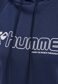 Marinblå huvtröja i mjukt tyg med en stor vit logotyp och text, justerbara snoddar vid huvan och minimala sömnadsdetaljer.