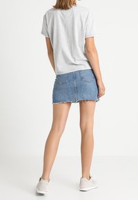 Grå bomull t-shirt kombinerad med en blå denim mini kjol. Kjolen har fransad nederkant, fickor och en figurnära silhuett. Bärs med ljusgrå sneakers.