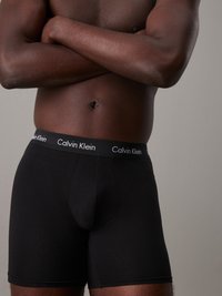 Crne pamučne bokserice s prilagođenim dizajnom i elastičnim pojasom na kojem se nalazi "Calvin Klein" logo u bijeloj boji. Standardne duljine i teksture.