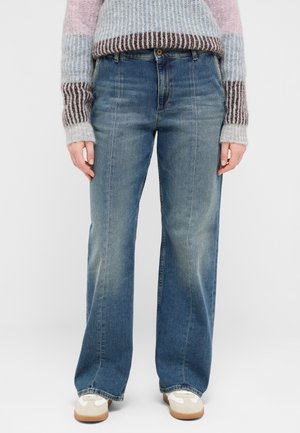 Person wearing wide-leg, faded blue jeans, a multicolored striped knit sweater, and white sneakers with beige accents.