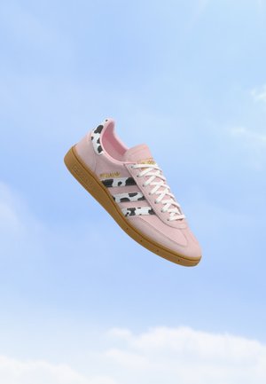 Ružové semišové tenisky Adidas s pásmi v potlači kravy a gumovou podrážkou, vznášajúce sa na pozadí jasnej modrej oblohy.