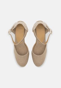 Beige espadriller med en teksturert stoffoverdel, ankelstropp med vevd detaljer, og rund tådesign. Flat såle i naturfiber.