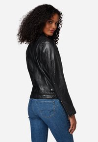 Svart läderjacka med räfflad axeldesign, figursydd siluett och dragkedjeärmar, i kombination med blå denimjeans.