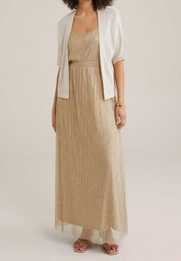 Třpytivé zlaté maxi šaty s přiléhavým živůtkem a plisovanou sukní, doplněné lehkým třpytivým kardiganem. Celý outfit dokončují nízké sandály.