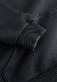 Dunkelgrauer Sweatshirt-Ärmel mit geripptem Bündchen, das auf dem passenden Stoff des Sweatshirt-Körpers liegt.