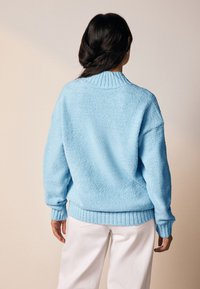 Sinine pehme kampsun soonikkoelise kaeluse ja varrukaäärtega, millel on lõdvestunud lõige ja tekstuuriga kangas. Kandmiseks valgete pükstega neutraalsel taustal.