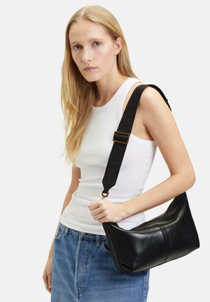 Sac à bandoulière en cuir noir avec une forme incurvée et une fermeture éclair. Il dispose d'une large bandoulière avec des lettres en relief et des garnitures en ton or.