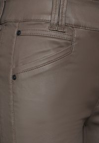 Bruna fusk läderbyxor har sidofickor, synlig sömnad och en slät yta. Svarta metallaccenter förbättrar designen.