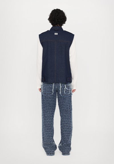 Denim vest in dark blue with a collar, shoulder seams, and two rear straps. Textured, frayed blue patterned pants with side pockets.