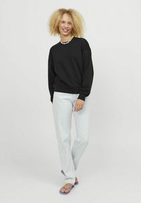 Felpa nera con colletto rotondo e maniche lunghe, abbinata a jeans dritti blu chiaro e infradito viola. Texture liscia.