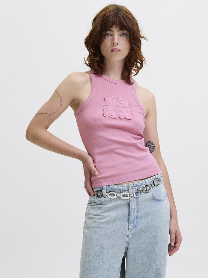 Rosa geripptes Tanktop mit strukturiertem Logodetail auf der Brust, kombiniert mit hellblauen High-Waist-Jeans und einem silbernen Kettengürtel.