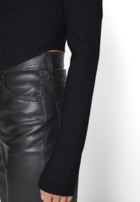 Schwarzes Langarmoberteil mit glatter Textur und figurbetonendem Schnitt, kombiniert mit hochtaillierten schwarzen Lederhosen mit glänzendem Finish und gesteppten Taschen.