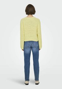 Maglione giallo con texture, maniche lunghe, scollatura rotonda e vestibilità corta, abbinato a jeans blu a gamba dritta e scarpe beige.
