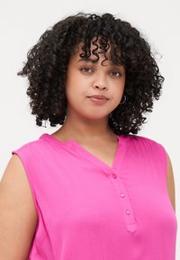 Blusa senza maniche fucsia con finitura testurizzata, caratterizzata da un collo a V e tre bottoni decorativi davanti.