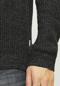 Donkergrijs gebreid sweater met een geribbelde textuur, met een klein merketiket aan de zijkant en een aansluitend manchetontwerp.