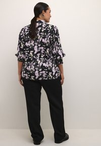 Bluse mit floralem Druck in Schwarz, Creme und Lavendel, mit Dreiviertelärmeln und elastischen Bündchen, kombiniert mit schwarzen, weit geschnittenen Hosen.