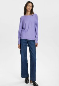 Lila långärmad stickad tröja med vid halsringning, tillsammans med mörkblå raka jeans och svarta ankelstövlar.