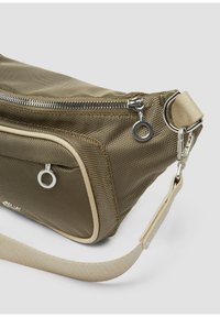 Khaki torba na ramię z siateczki z metalowymi elementami w kolorze srebrnym, wyposażona w górny zamek błyskawiczny, przednią kieszeń i beżowy pasek. Teksturowana powierzchnia, elegancki design.