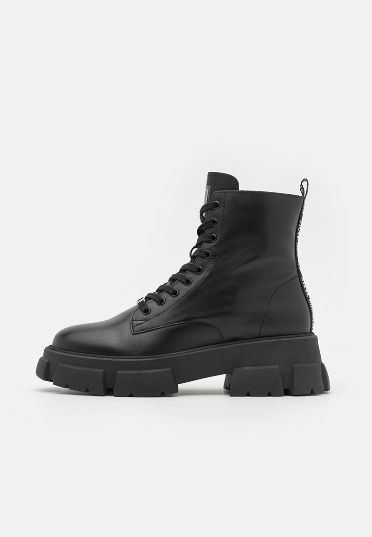Schwarze Leder-Schnürstiefel mit einer robusten schwarzen Gummisohle, hohem Knöchel und einer Schlaufe an der Rückseite; minimalistisches Design und strukturierte Oberfläche.