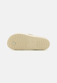 Suola di scarpa in gomma beige con motivo testurizzato, caratterizzata da creste rialzate e un'impronta circolare del logo per aderenza e stabilità.