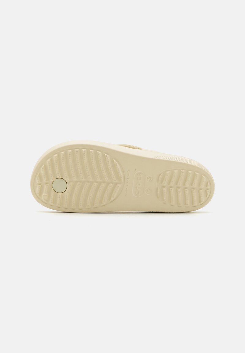 Beige Gummisohle mit strukturiertem Muster, ausgestattet mit erhöhten Rillen und einem runden Logoabdruck für Traktion und Stabilität.