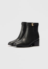 Sorte skinn ankle boots med rund tå og blokkhel. Har et dekorativt belte med gullfiner ved ankelen. Smidig tekstur.