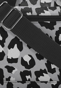 Bolsa de tela gris con un patrón de estampado animal en blanco y negro, con una correa ajustable negra y detalles de metal.