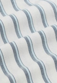 Hvidt stof med jævnt fordelte lodrette blå og sorte striber, vist i bløde folder, der fremhæver tekstur og mønster.