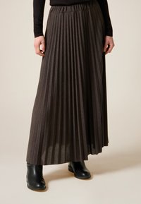 Plisserad lång brun kjol i texturerat tyg med en rynkad midjeresår. Kombineras med svarta ankelstövlar.