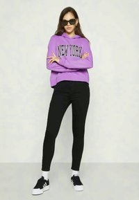 Hanorac mov cu textul "NEW YORK", colanți negri și adidași negri. Îmbrăcămintea are o croială confortabilă și un design modern.