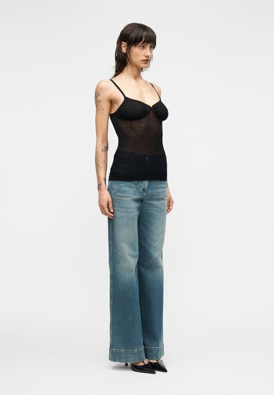 Μαύρο διαφα νές τοπ με λεπτές τιράντες, συνδυασμένο με ανοιχτό μπλε τζιν παντελόνι φαρδιάς γραμμής. Η εμφάνιση χαρακτηρίζεται από λεπτή υφή και εφαρμοστή σιλουέτα.