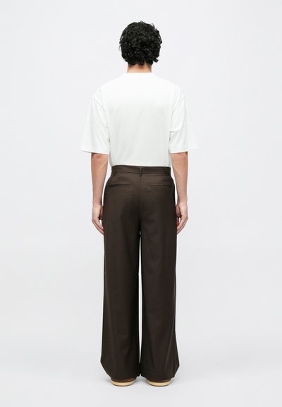 Valge lühikeste varrukatega t-särk ja pruunid laiade säärtega püksid, mis on sileda tekstuuriga, klassikalise lõikega ja varjatud tagataskutega.