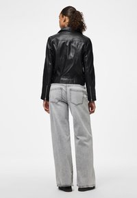 Must have naha nahkjope sobiva kujundusega, terava kraega ja tõmblukkudega varrukatel; koos hallide laia säärega teksade ja mustade kingadega.