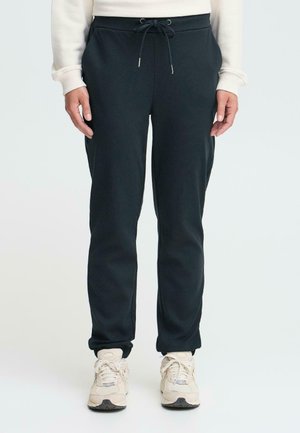 Sorte joggebukser med snor i livet, smal passform og elastiske mansjetter, laget av et mykt stoff. Brukt med lysfargede sneakers.