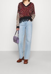 Maglione rosso e nero con motivo a righe e maniche lunghe in stampa leopardata, rifinito con pizzo. Jeans a gamba dritta blu chiaro e scarpe con tacco quadro marroni. Borsa viola.