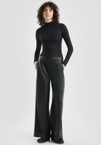 Dopasowany czarny top z długim rękawem łączy się z szerokimi, czarnymi spodniami z ekoskóry z guzikami, tworząc elegancki, monochromatyczny strój.