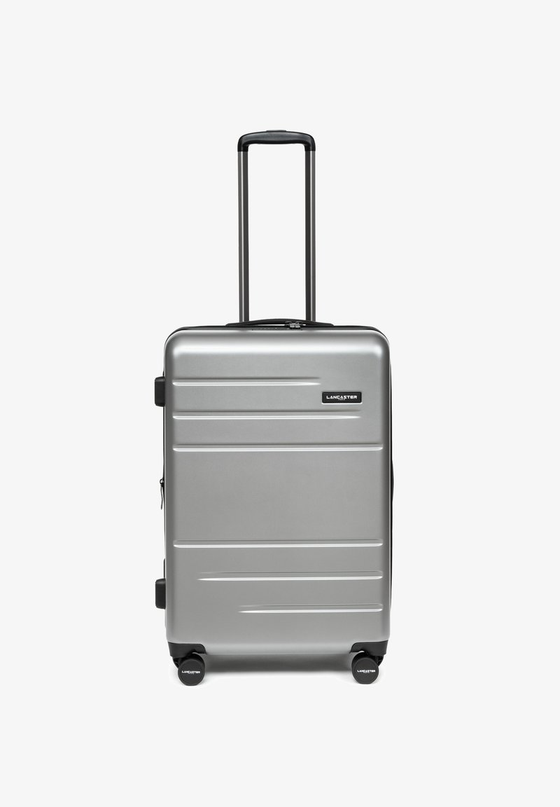 Valise rigide argentée avec poignée télescopique noire et quatre roues pivotantes noires, portant la marque "Lancaster" sur le devant.