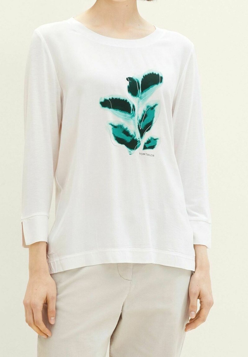 Camicia bianca a maniche lunghe con stampa di foglie verdi sul petto. Tessuto morbido e leggero con una vestibilità rilassata e spacchi laterali all'orlo.